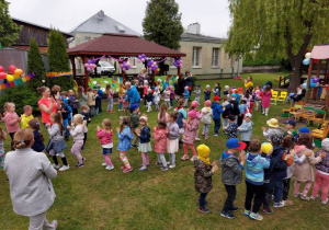 Dzieci klaszczą ustawione jedno za drugim w ogrodzie przedszkolnym